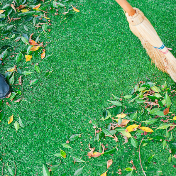 Working with a broom sweeps the lawn from the fallen leaves. The autumn season, working in the yard outdoors.